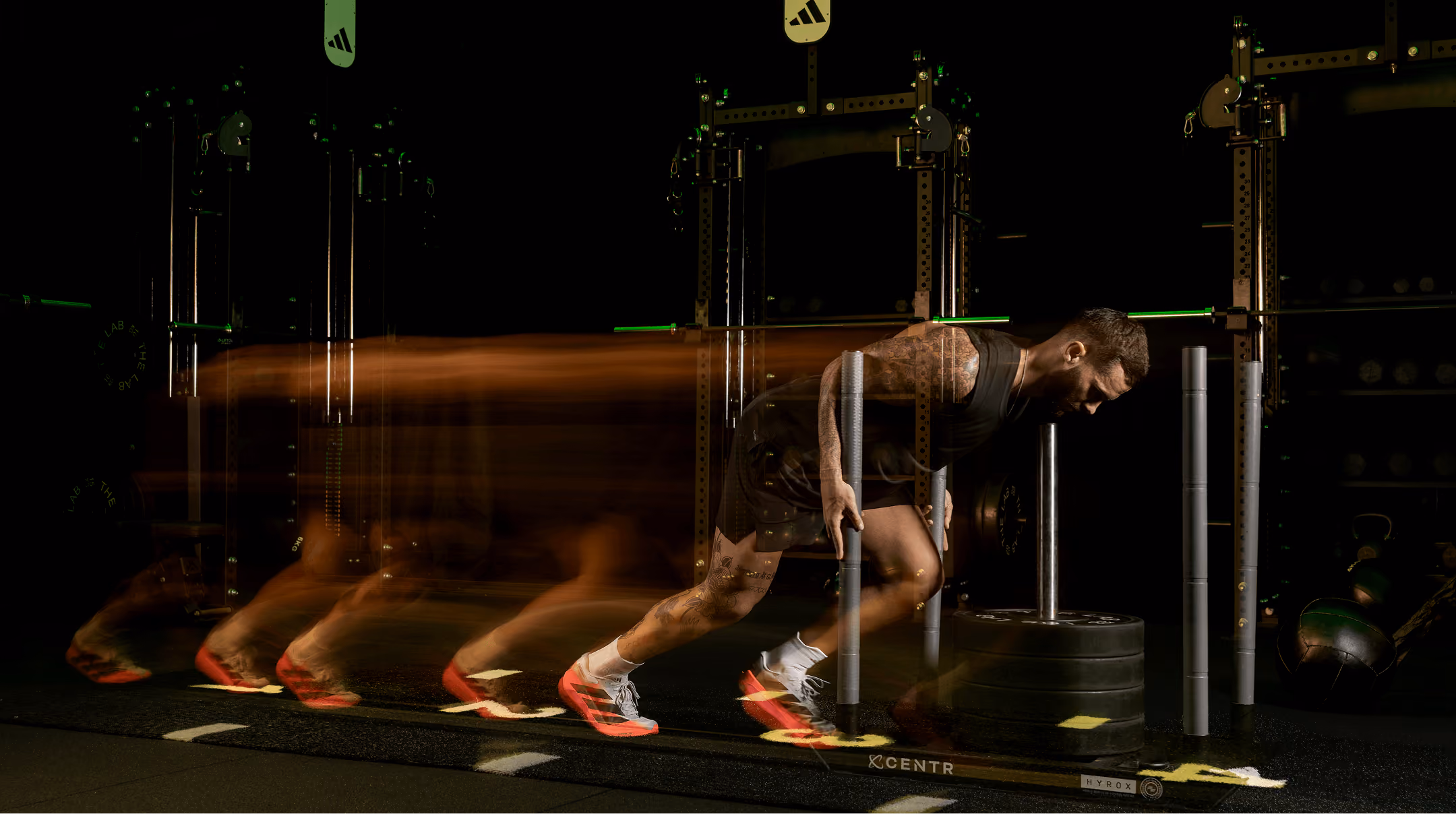 Athletic man with tattoos pushing a weighted sled in a gym, motion blur showing movement and effort.
