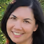 Smiling woman with long dark hair and light skin wearing a dark top, looking at the camera.