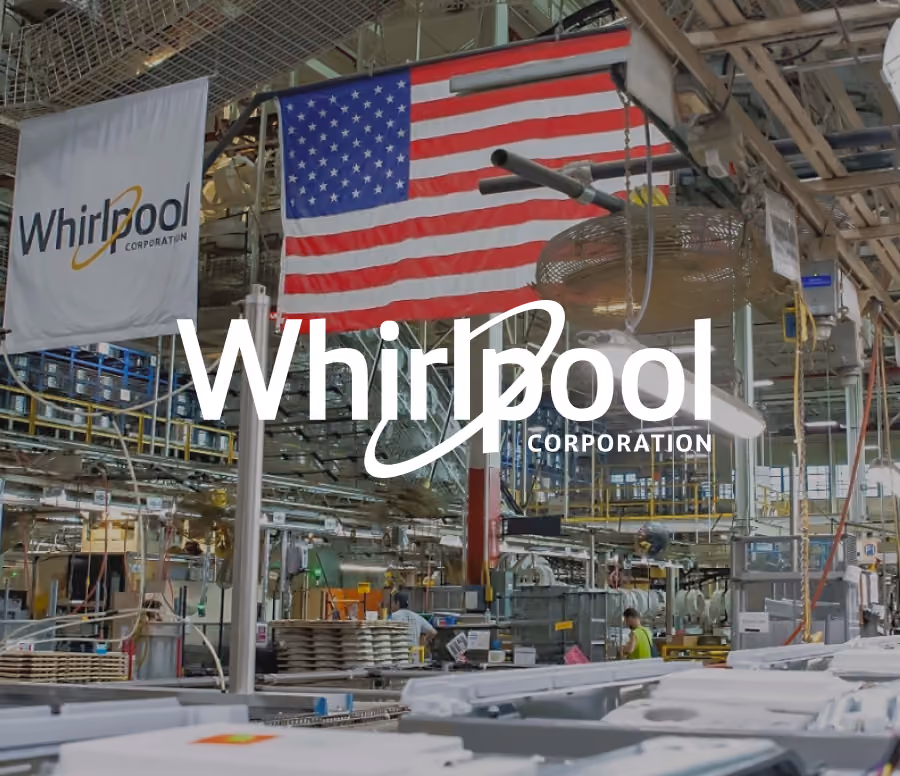Whirlpool Corporation logo overlaying a busy manufacturing factory floor with an American flag hanging overhead and workers operating machinery.