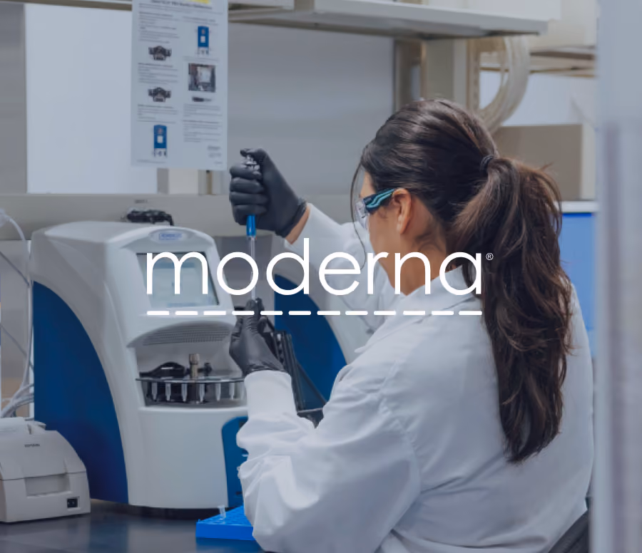 Scientist with long dark hair in a white lab coat and protective glasses uses a pipette in a laboratory with advanced equipment.