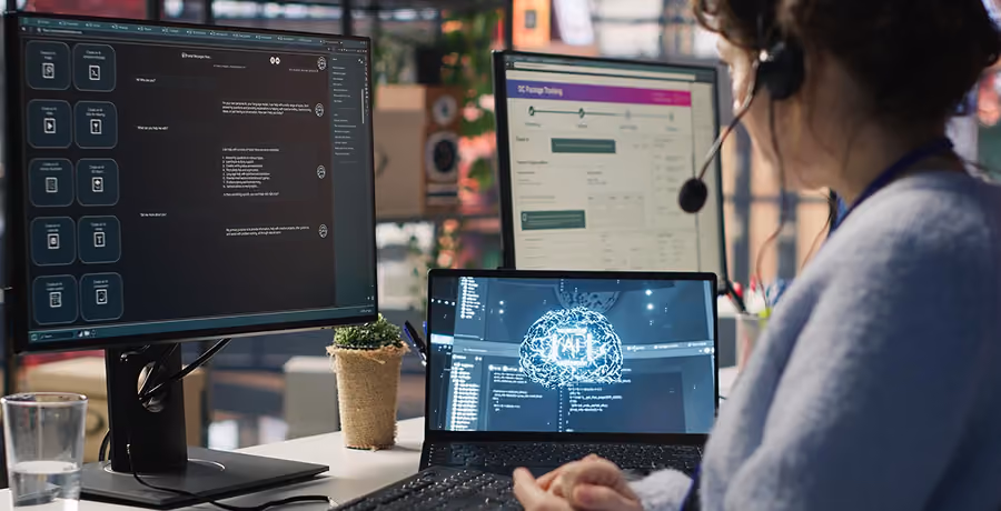 Person wearing a headset working at a desk with three screens displaying software code, a 3D brain graphic, and a package tracking webpage in a modern office setting.