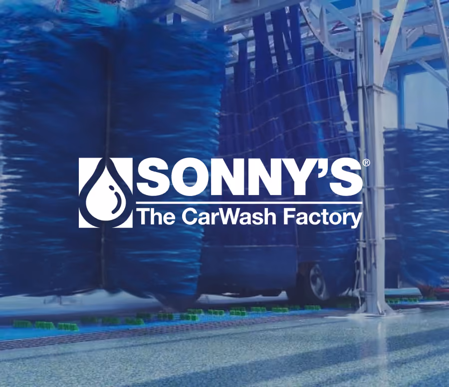 Inside view of an automated car wash with large blue rotating brushes cleaning vehicles, overlaid with the Sonny's The CarWash Factory logo in white.