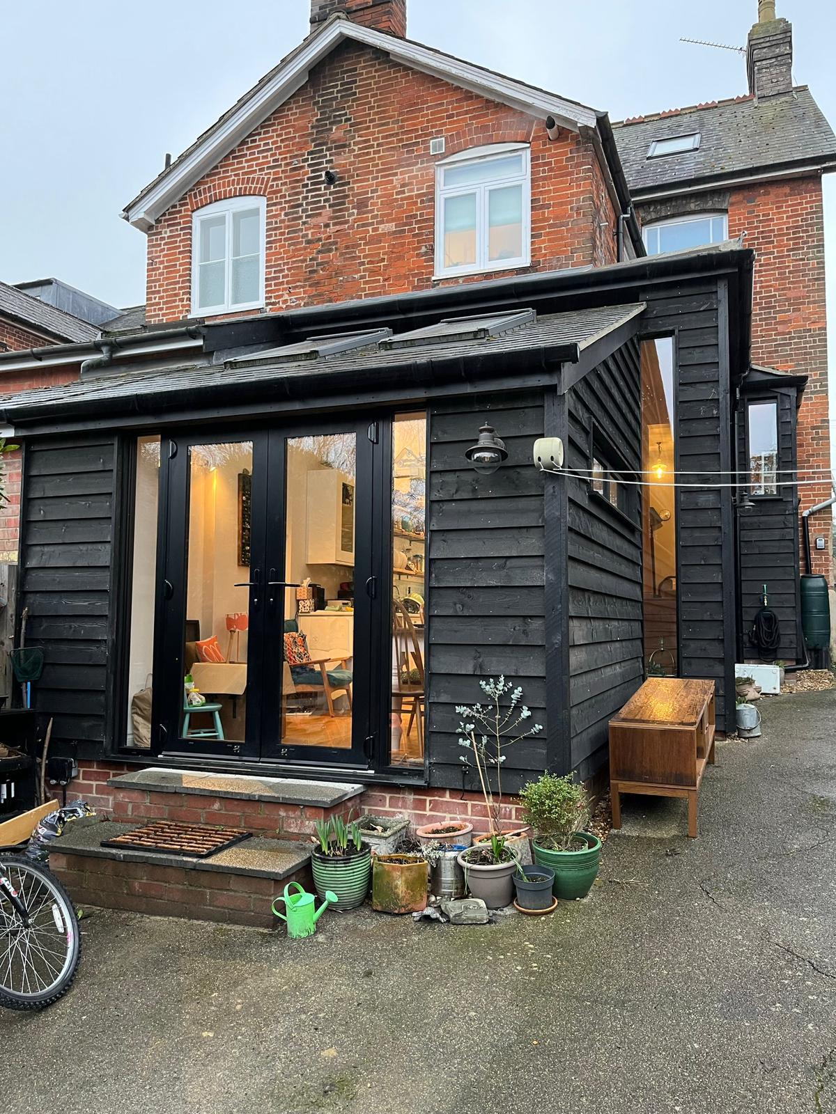 Rear extension with black timber cladding and large black-framed doors, lit at dusk