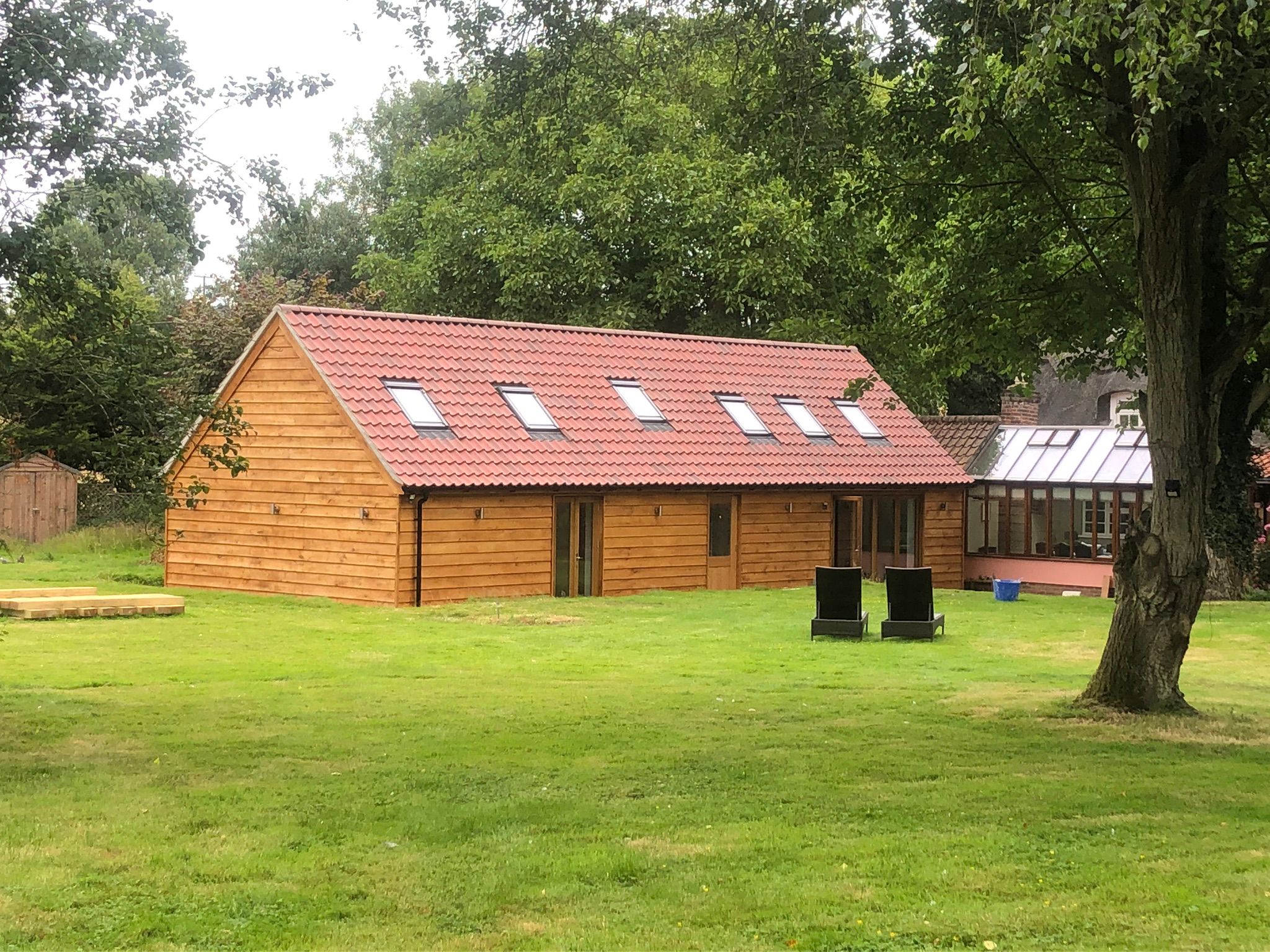 Completed timber-clad garden building with a traditional tiled roof and rooflights, set among mature trees