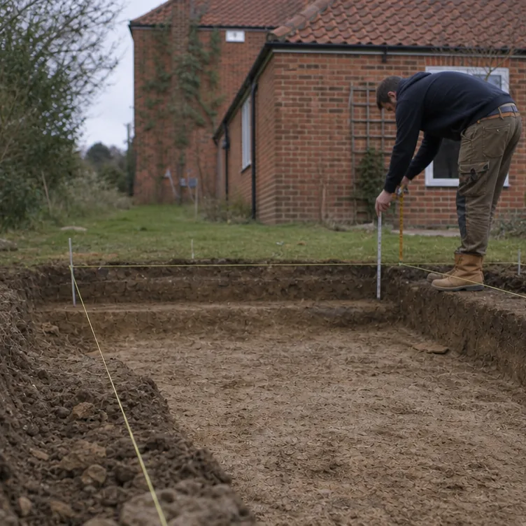 Builder checking levels over the foundation trench for a garden room at the end of a Bury St Edmunds garden