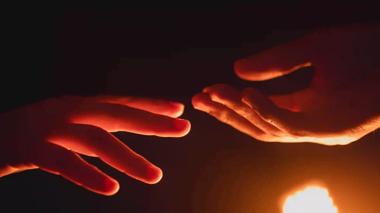 Two hands are reaching out in dim light, with one hand appearing to pull back slightly from the other. This visual represents a disconnect and defensive posture in a conversation.