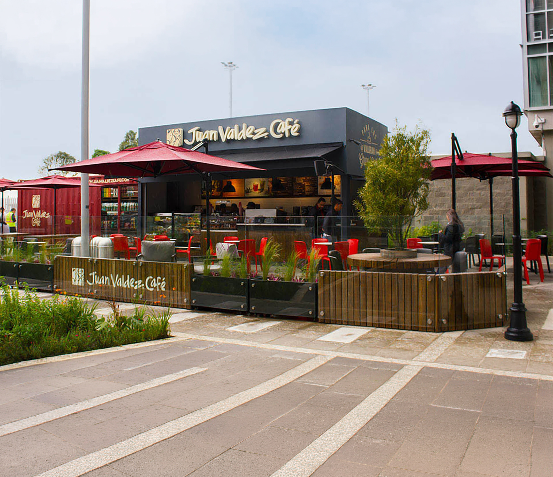Outdoor seating area of Juan Valdez Café with red umbrellas, red chairs, and people ordering coffee.