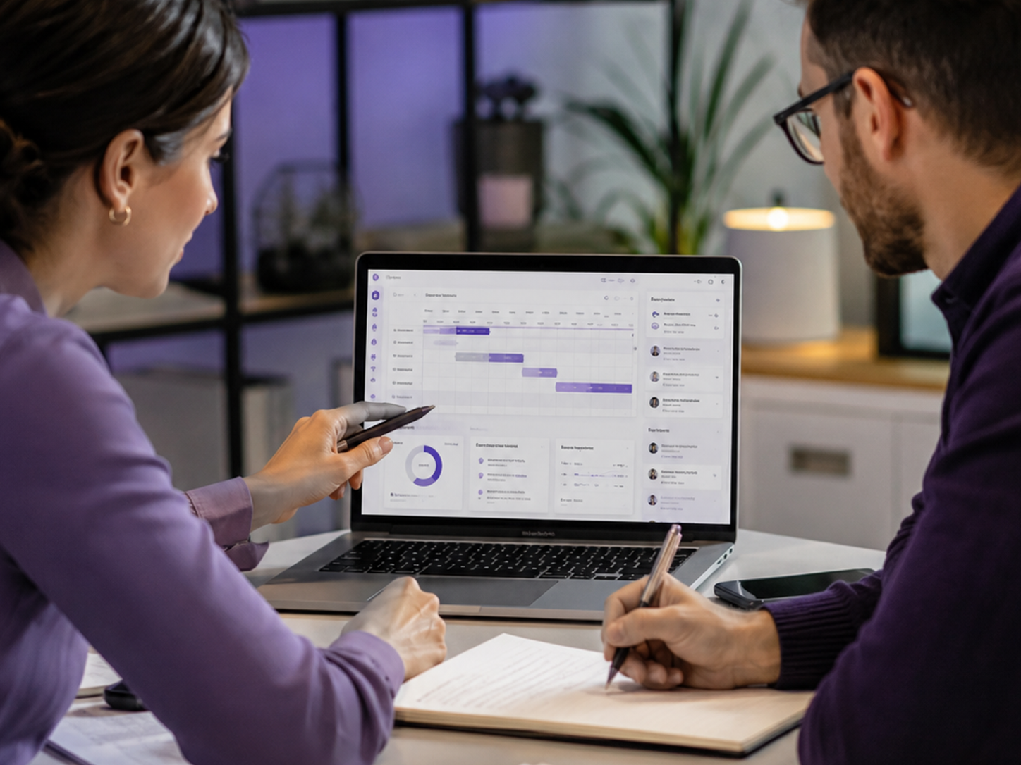 Two people reviewing a project timeline chart and data on a laptop during a meeting.