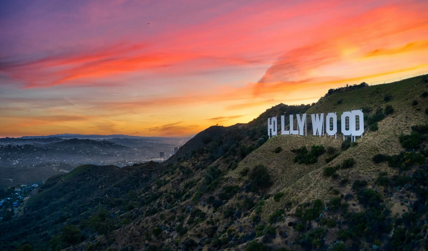 Hollywood sign on a brush-covered hillside under an orange and purple sunset sky