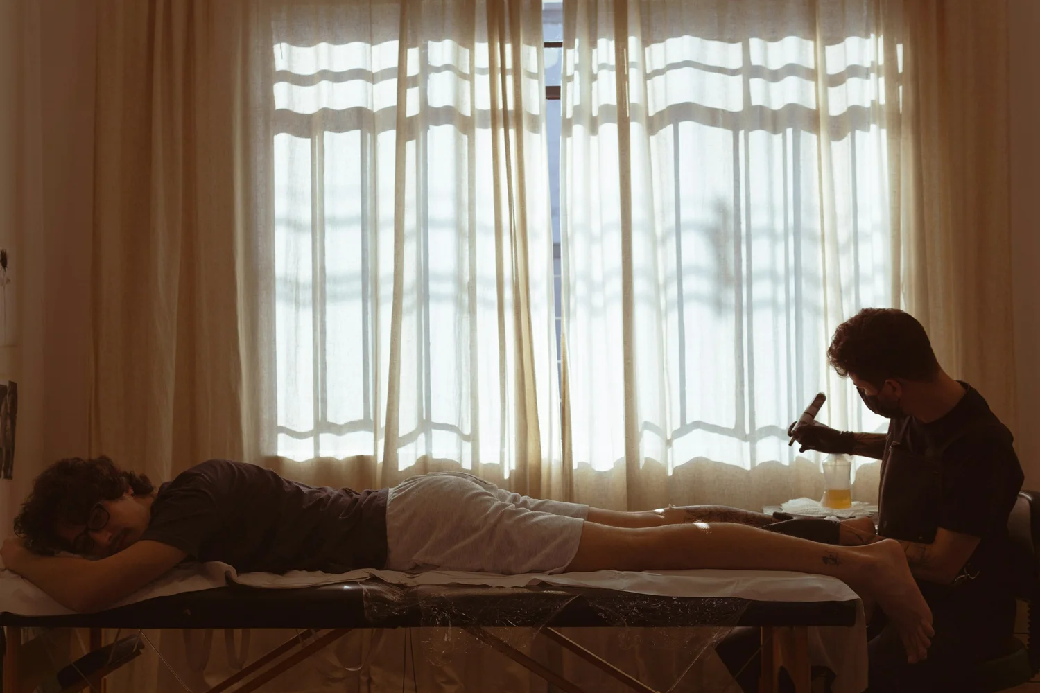 Person lying face down on a padded table while a seated person holds a handheld tool near their legs