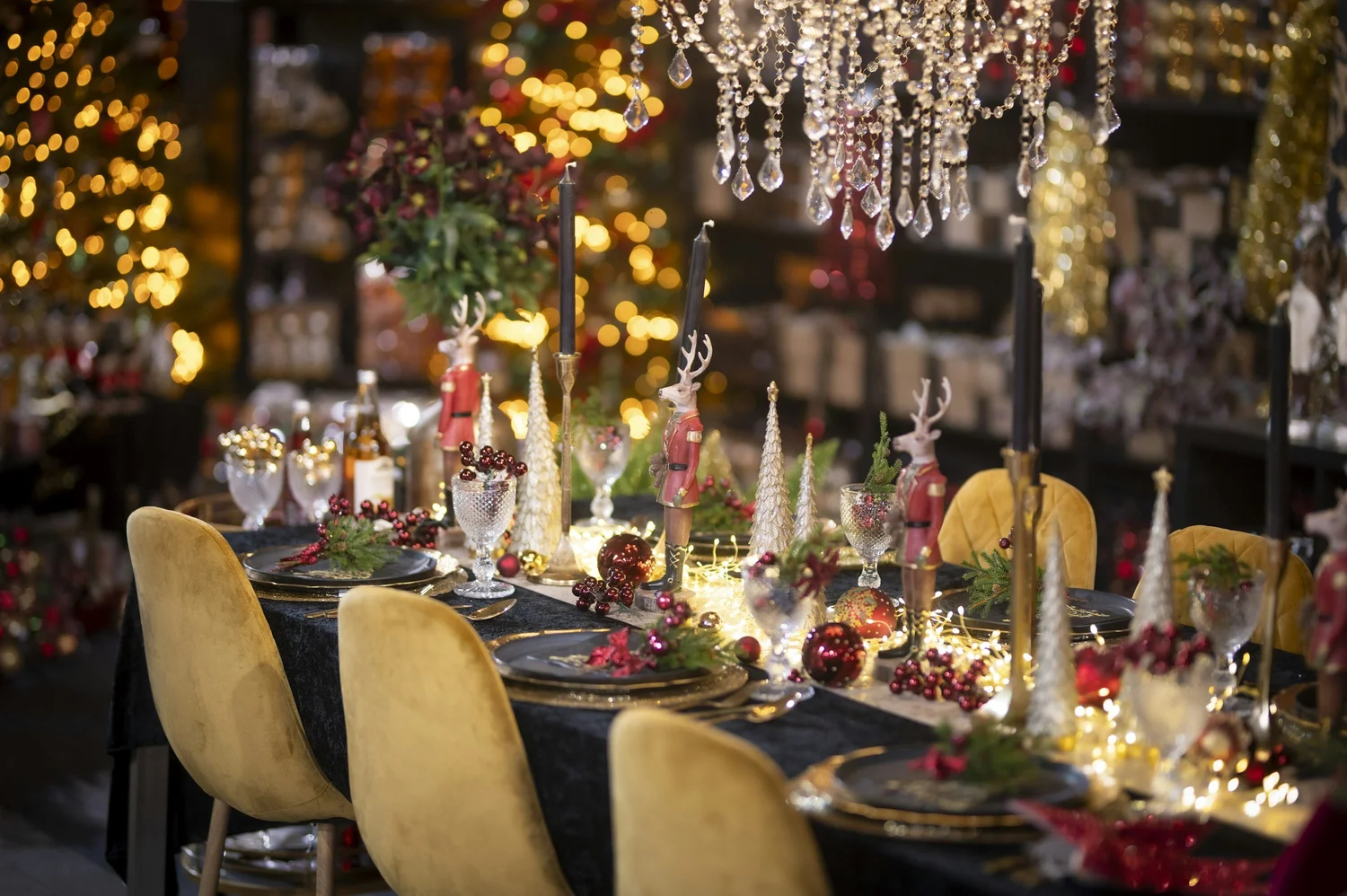 Decorated dinner table with candles, greenery and yellow velvet chairs beneath hanging crystal strands