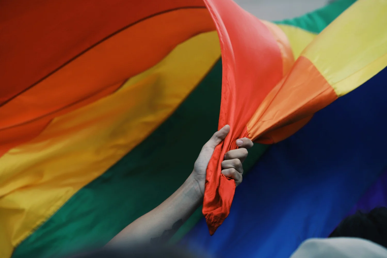 A hand gripping the edge of a large rainbow flag