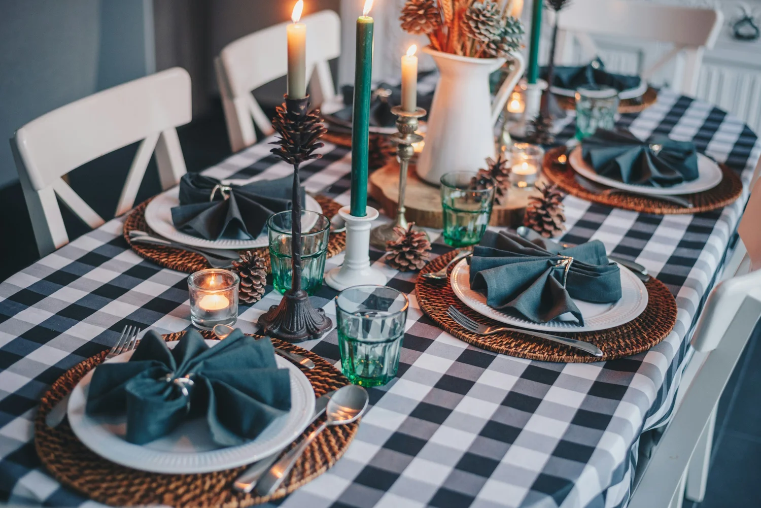 Table set with a checked tablecloth, woven placemats, folded napkins on white plates and lit candles