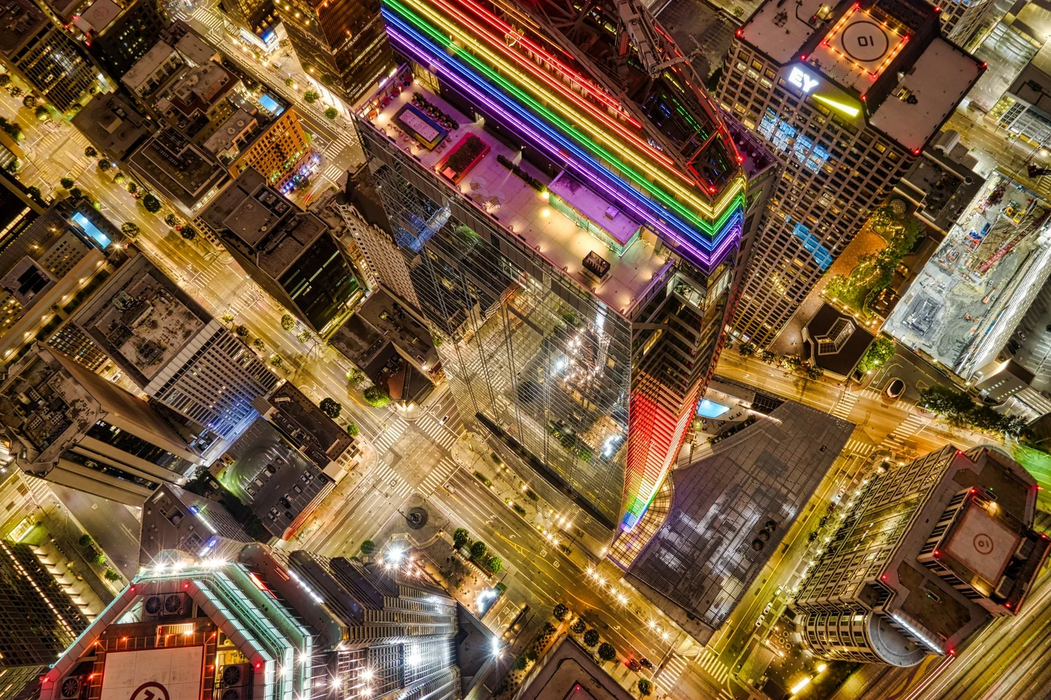 Aerial night view of city blocks and lit streets, with one tall building lit in rainbow stripes