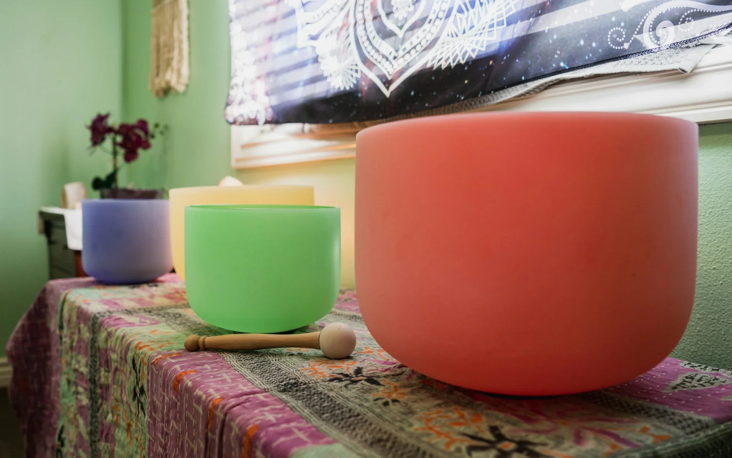 Frosted bowls in coral, green, purple and pale yellow with a wooden mallet on a patterned tablecloth