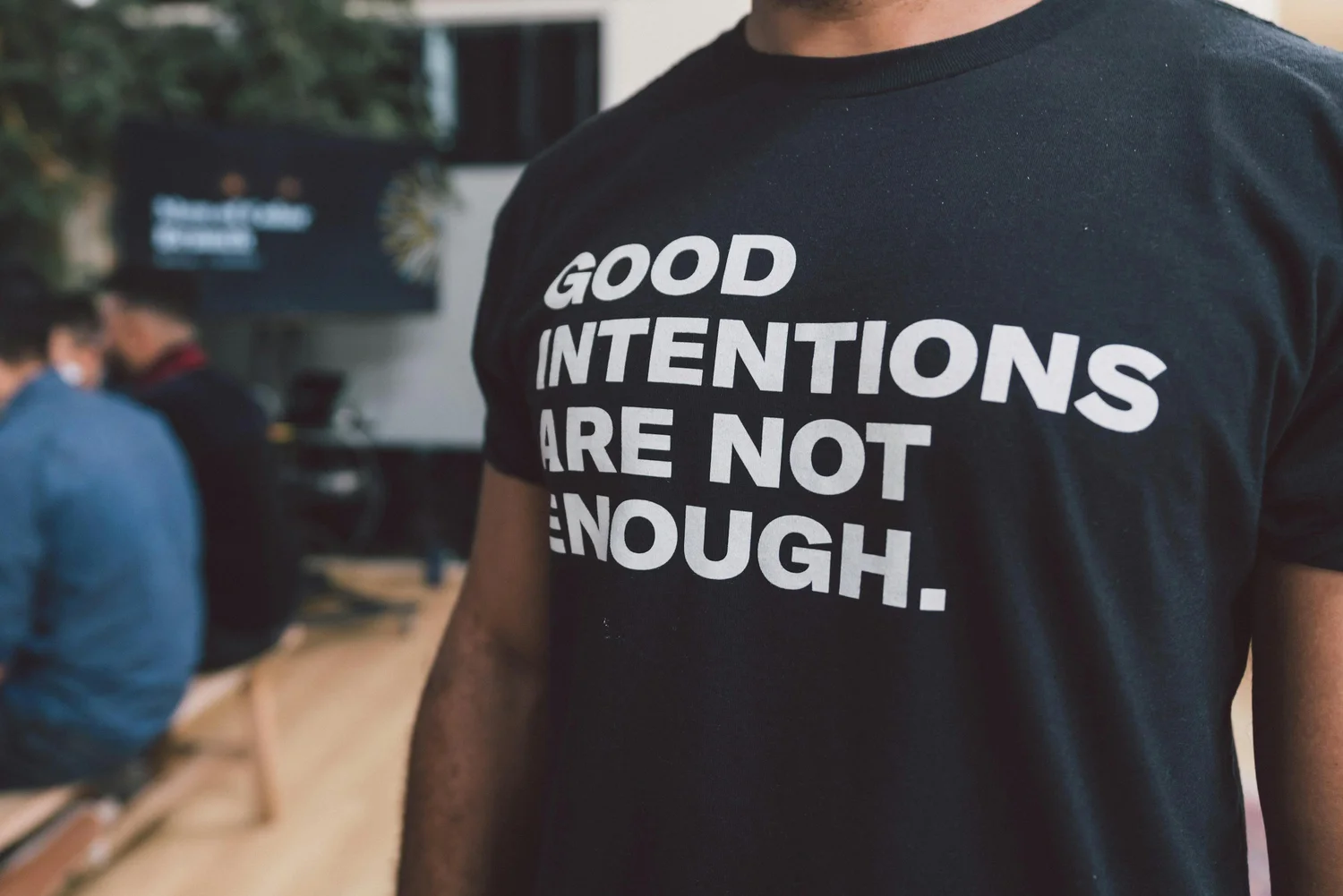 A person in a black T-shirt printed with the words "Good intentions are not enough"