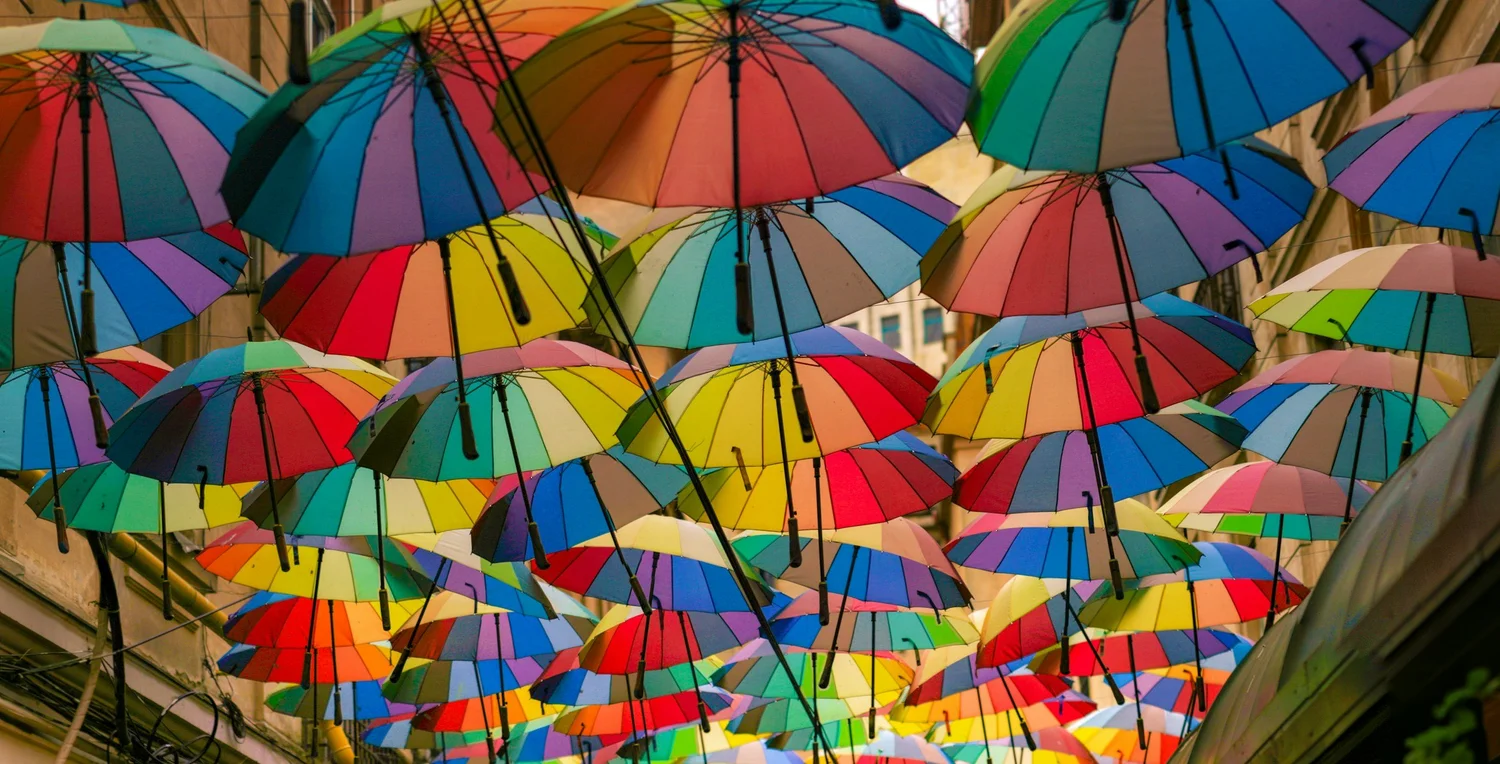 Dozens of rainbow-striped umbrellas hanging in the air between buildings