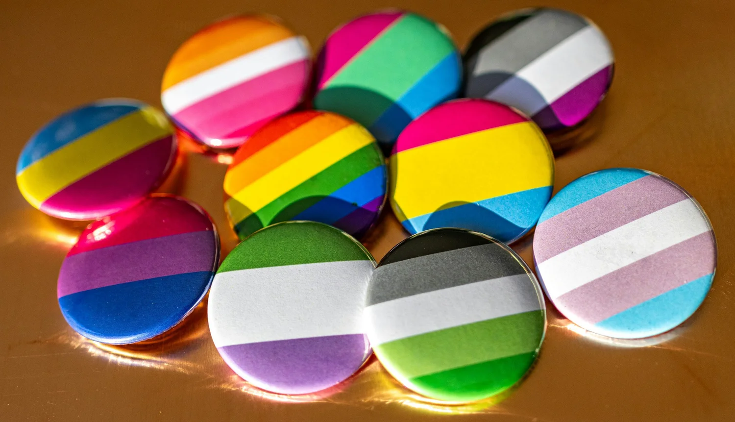 Round pin buttons printed with striped pride flag designs in many colors on a gold surface