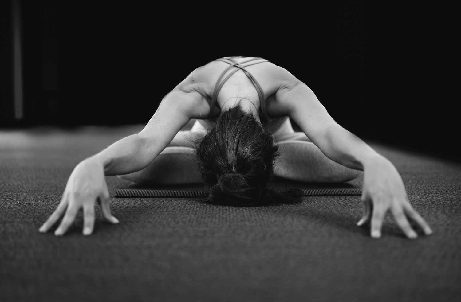 Black and white view of a person folded forward on a mat, head bowed, arms reaching to the floor