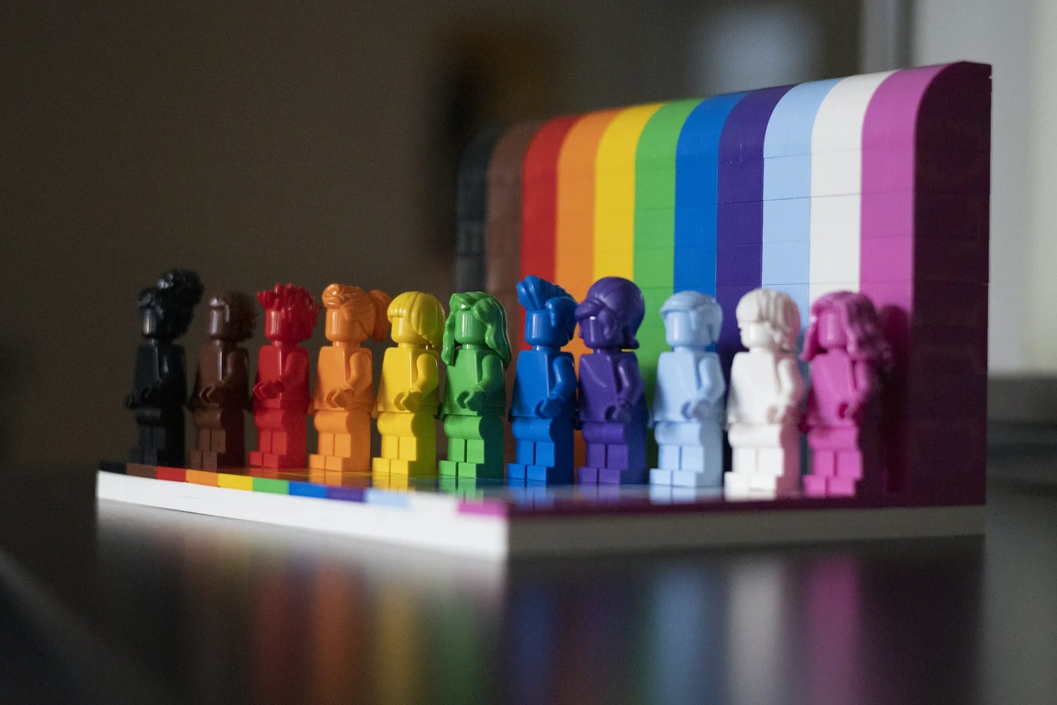 Row of toy figures in black, brown and rainbow colors in front of a matching striped backdrop