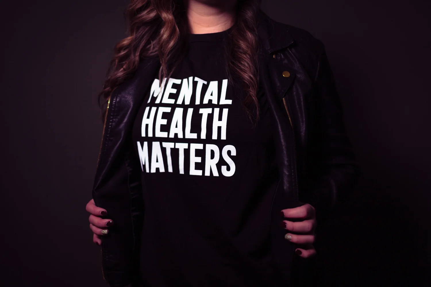 A person holds open a leather jacket over a black T-shirt printed "Mental health matters"