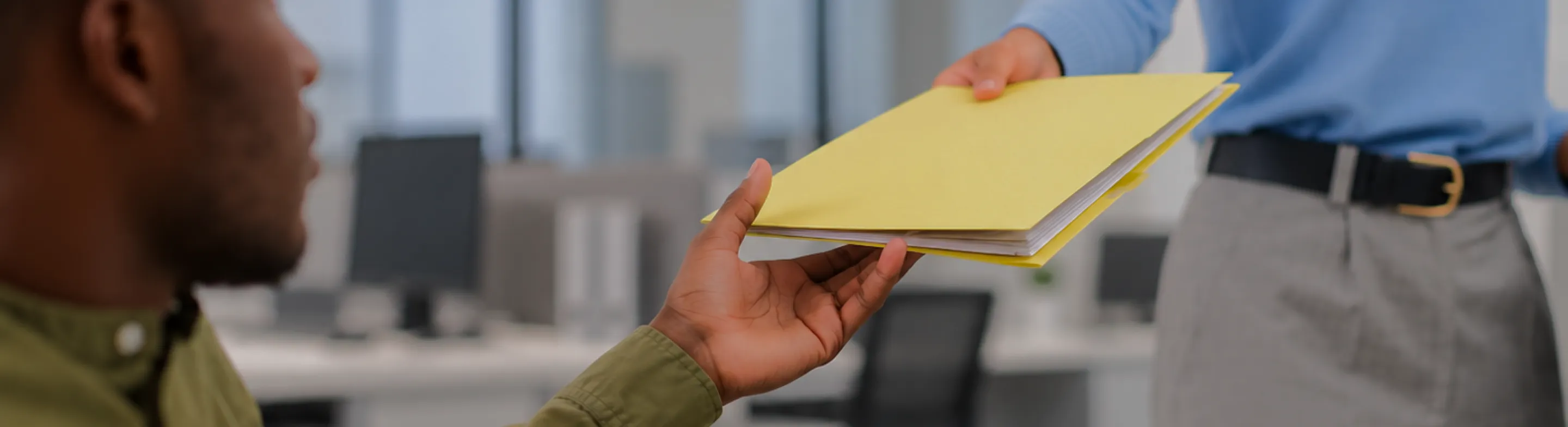 A yellow claim folder being handed across an office