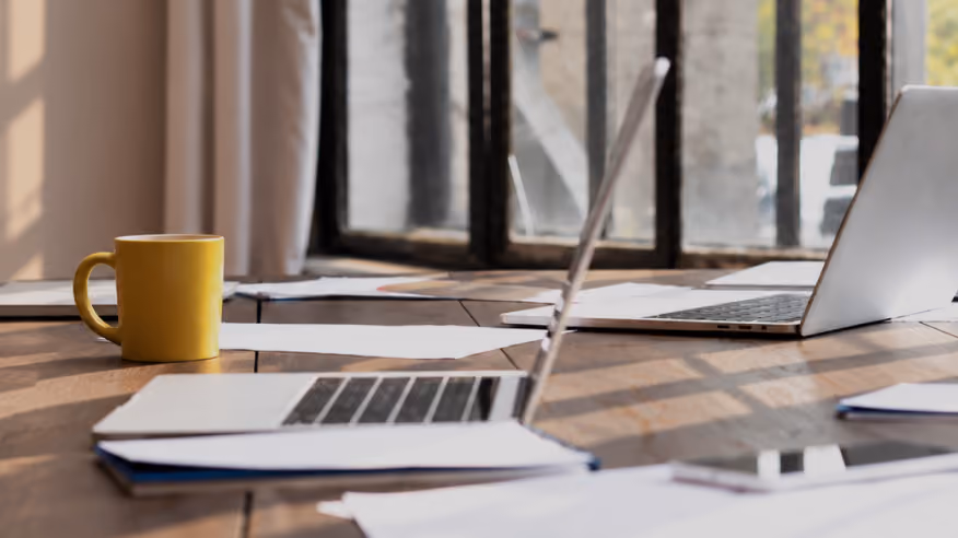 Open laptops and a yellow mug on a sunlit meeting table