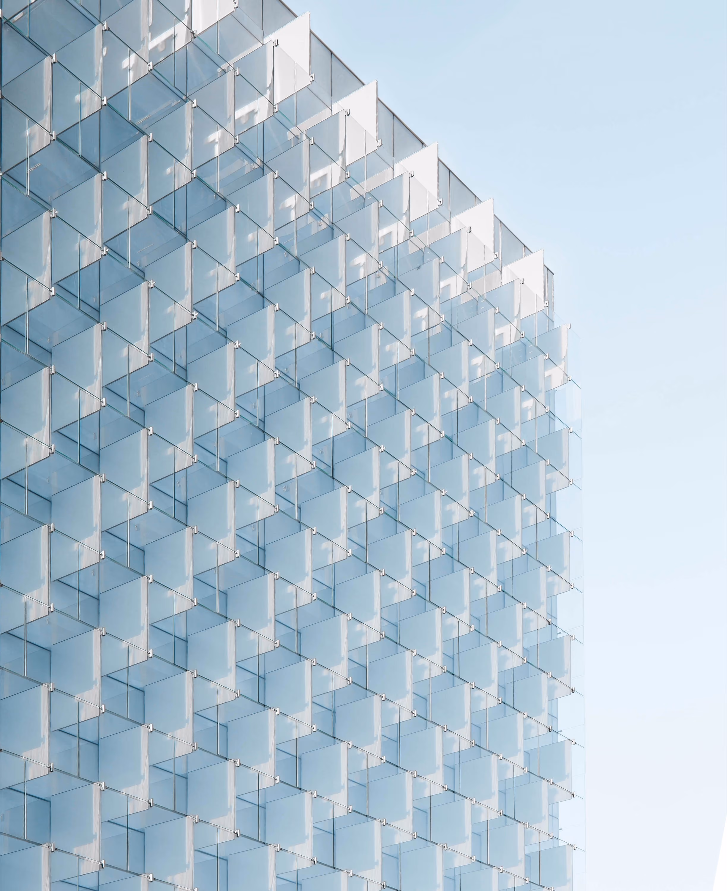 Fassadenansicht eines modernen Gebäudes mit einem Muster aus durchscheinenden, rechteckigen Glasplatten, die gleichmäßig an der Außenwand befestigt sind, vor einem blauen Himmel.