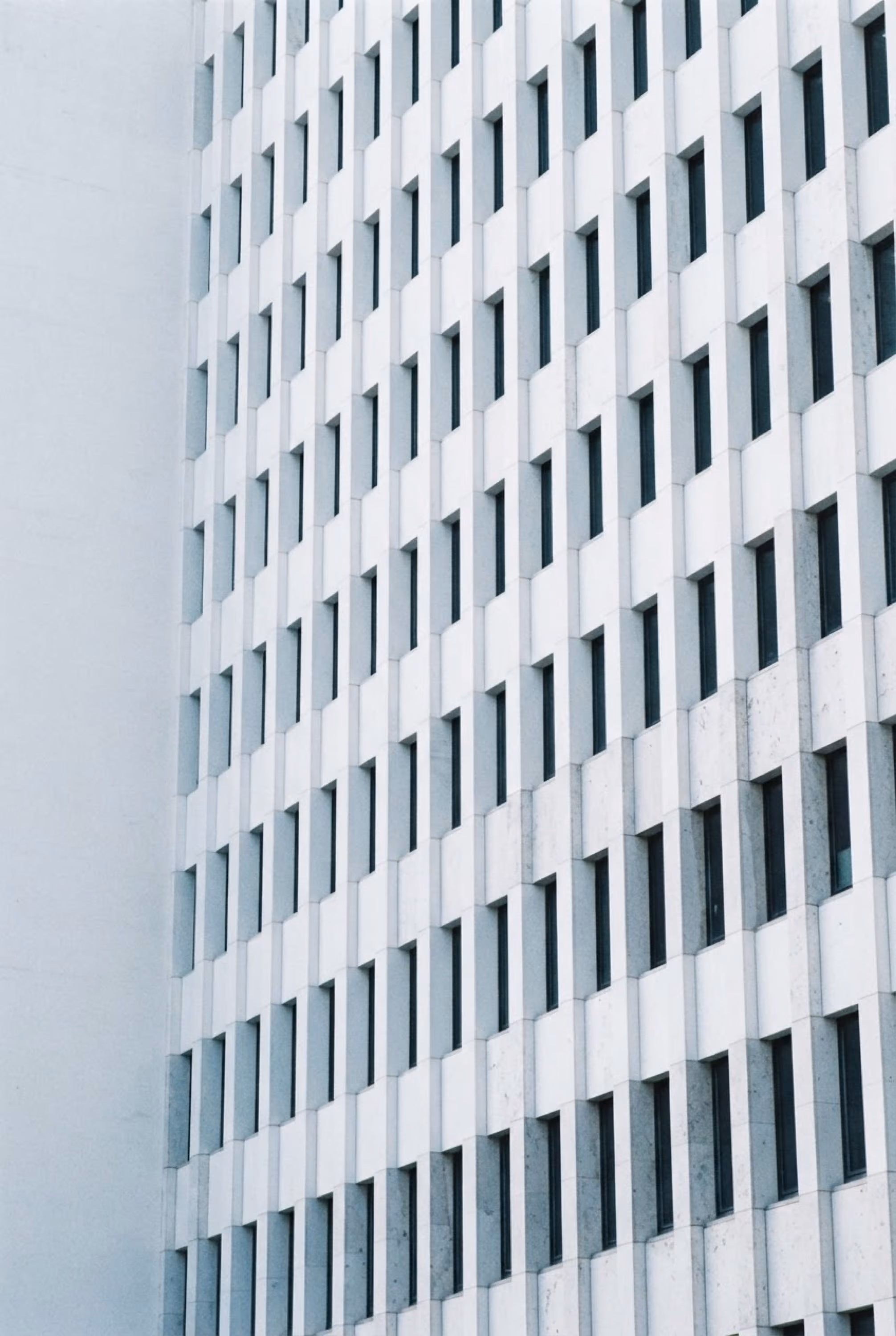 Fassade eines weißen Gebäudes mit zahlreichen symmetrisch angeordneten rechteckigen Fenstern.