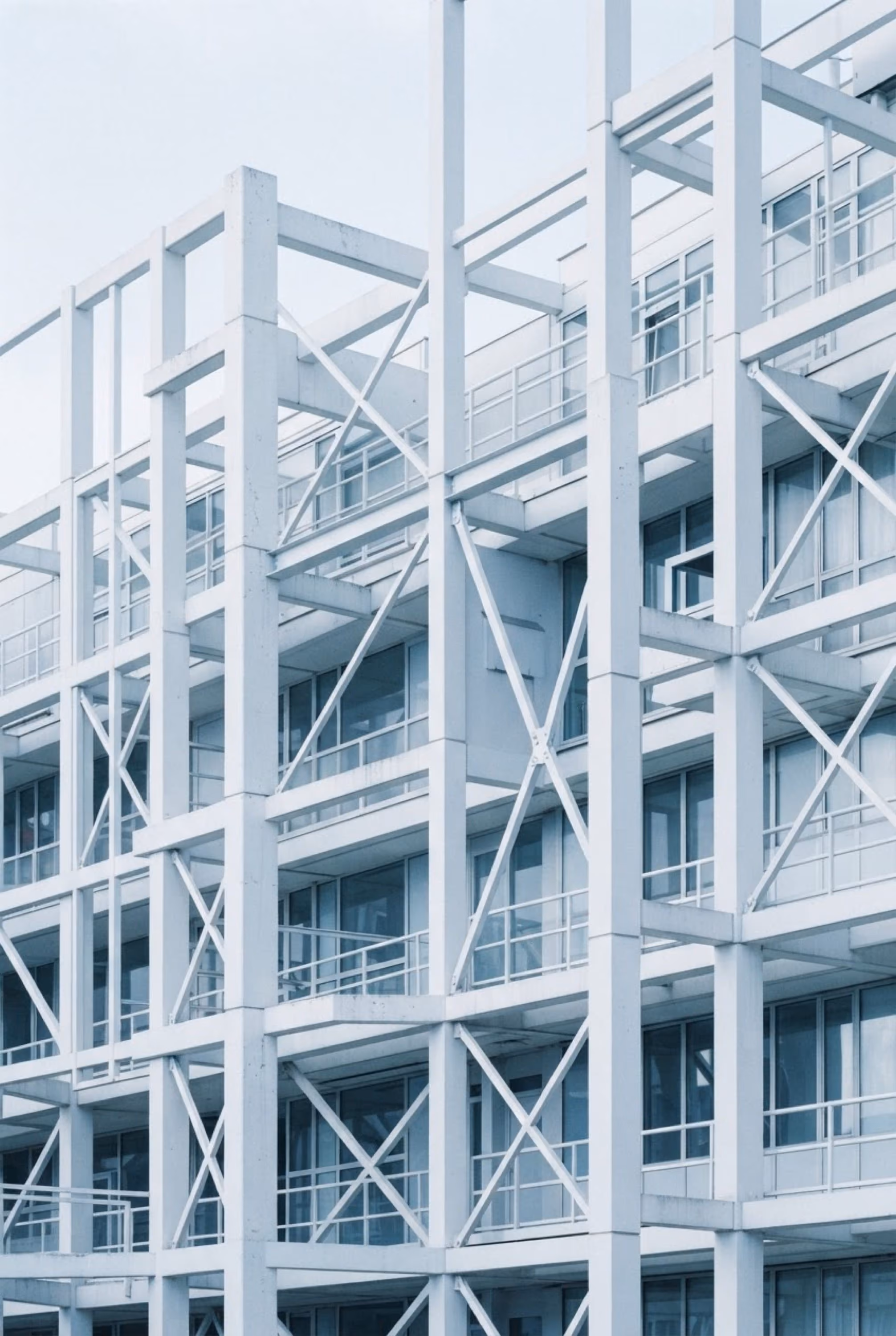 Nahaufnahme der weißen Stahlkonstruktion mit Querstreben eines modernen Gebäudes mit großen Glasfenstern und Balkonen.