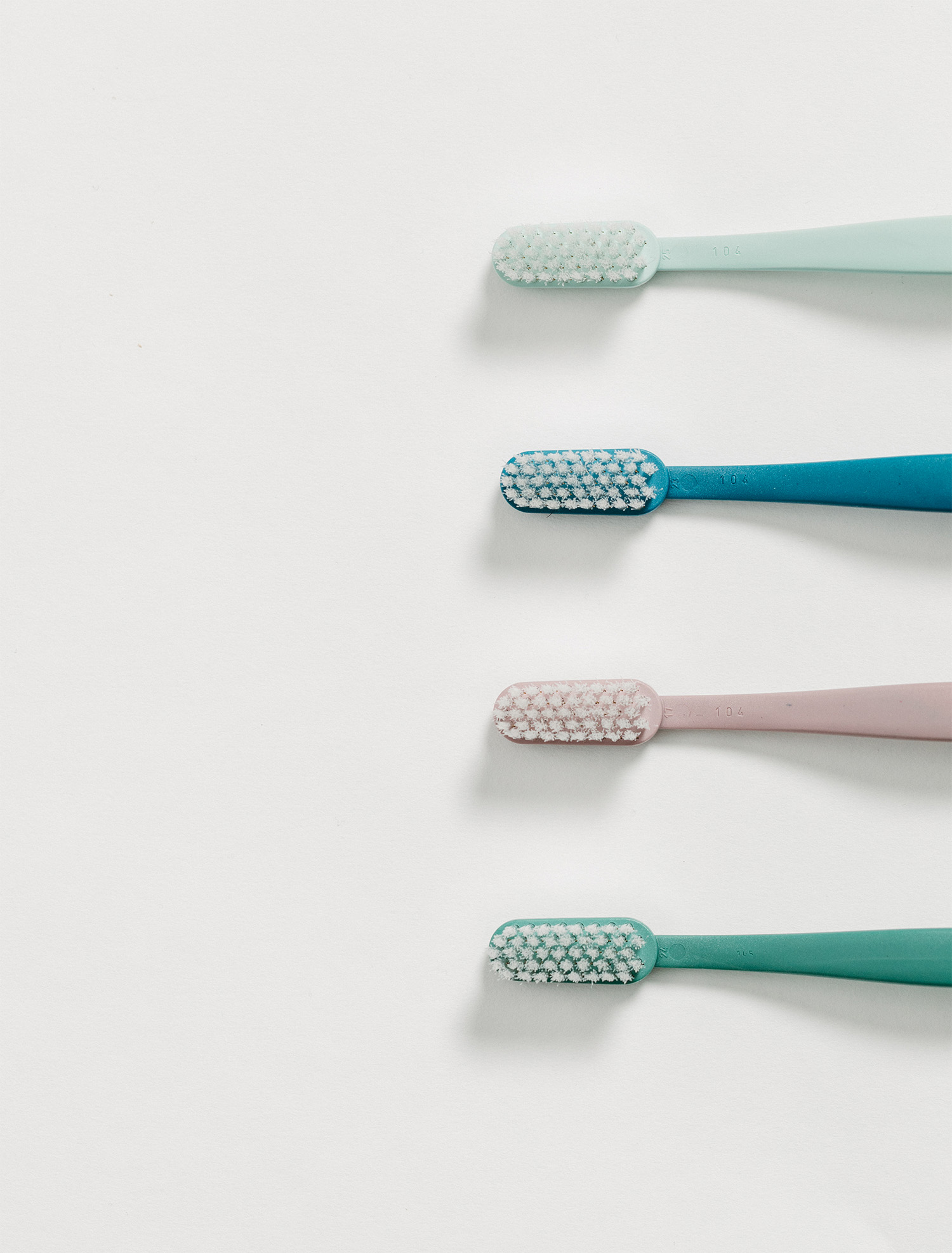 Toothbrush, toothpaste tube, and dental floss container on beige tiled surface.