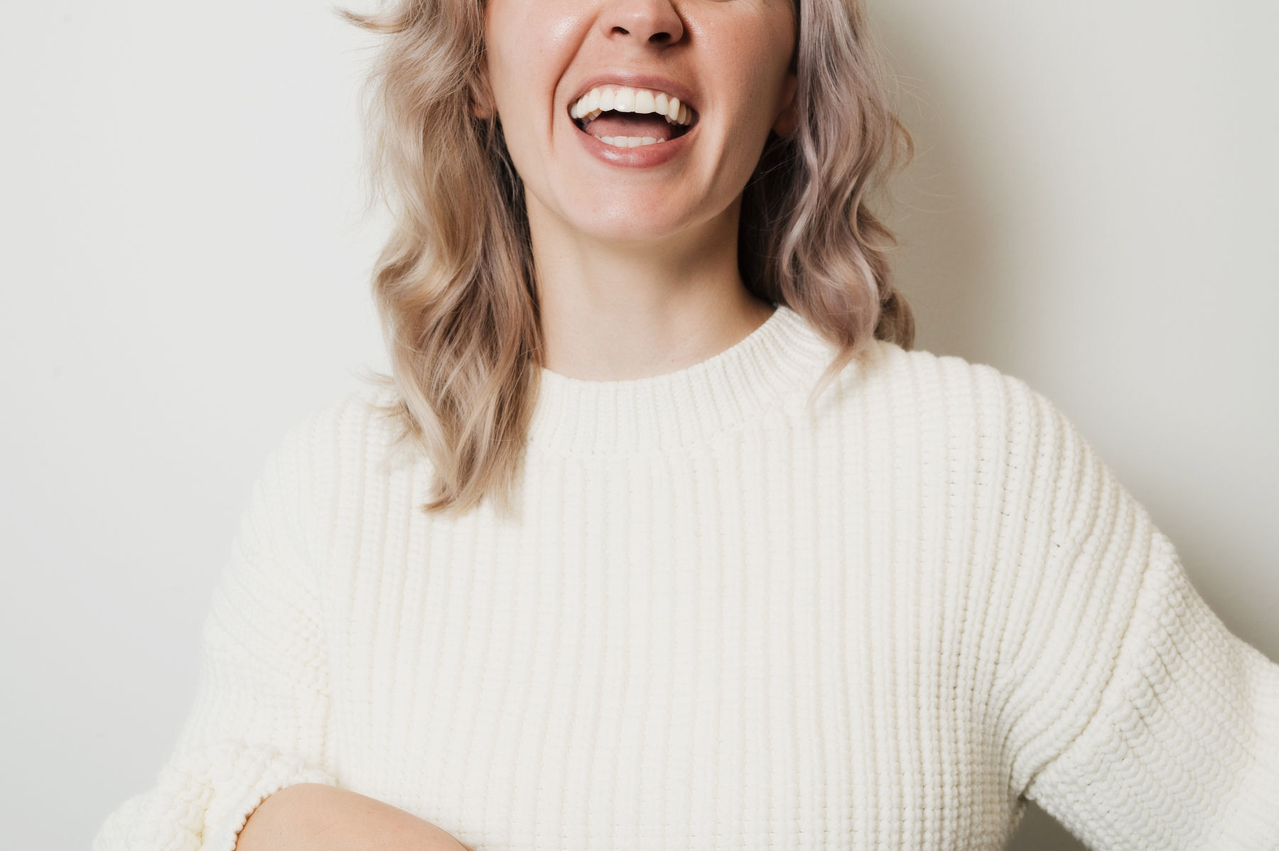 Woman in a cream sweater laughing with a bright smile