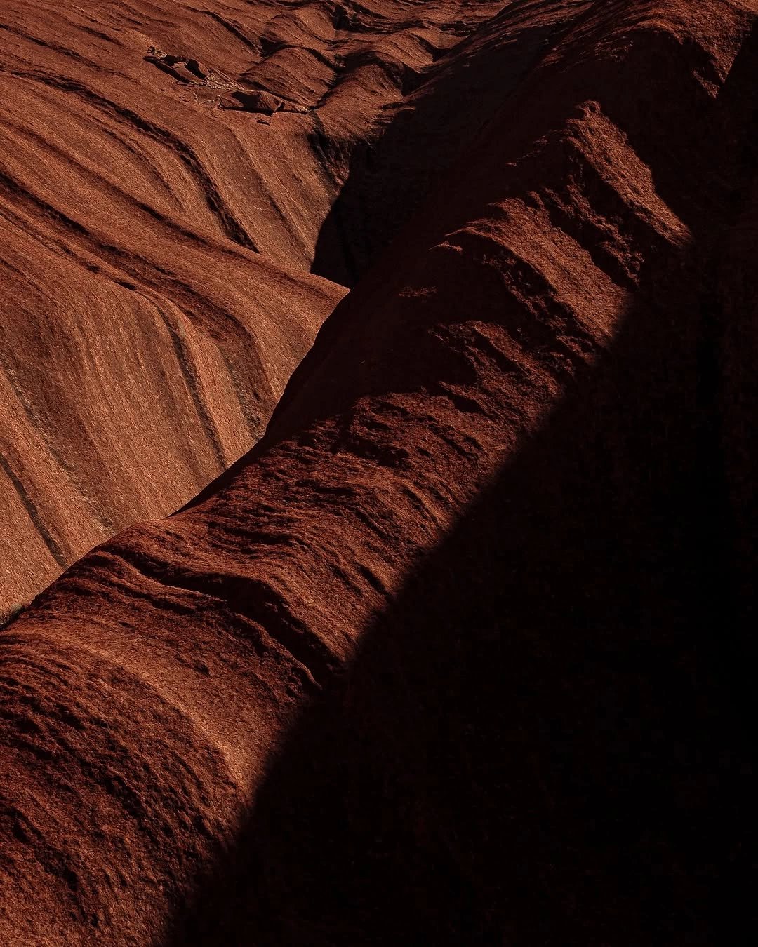 Vue rapprochée de formations rocheuses rouges avec des stries et ombres créant un contraste entre lumière et obscurité.