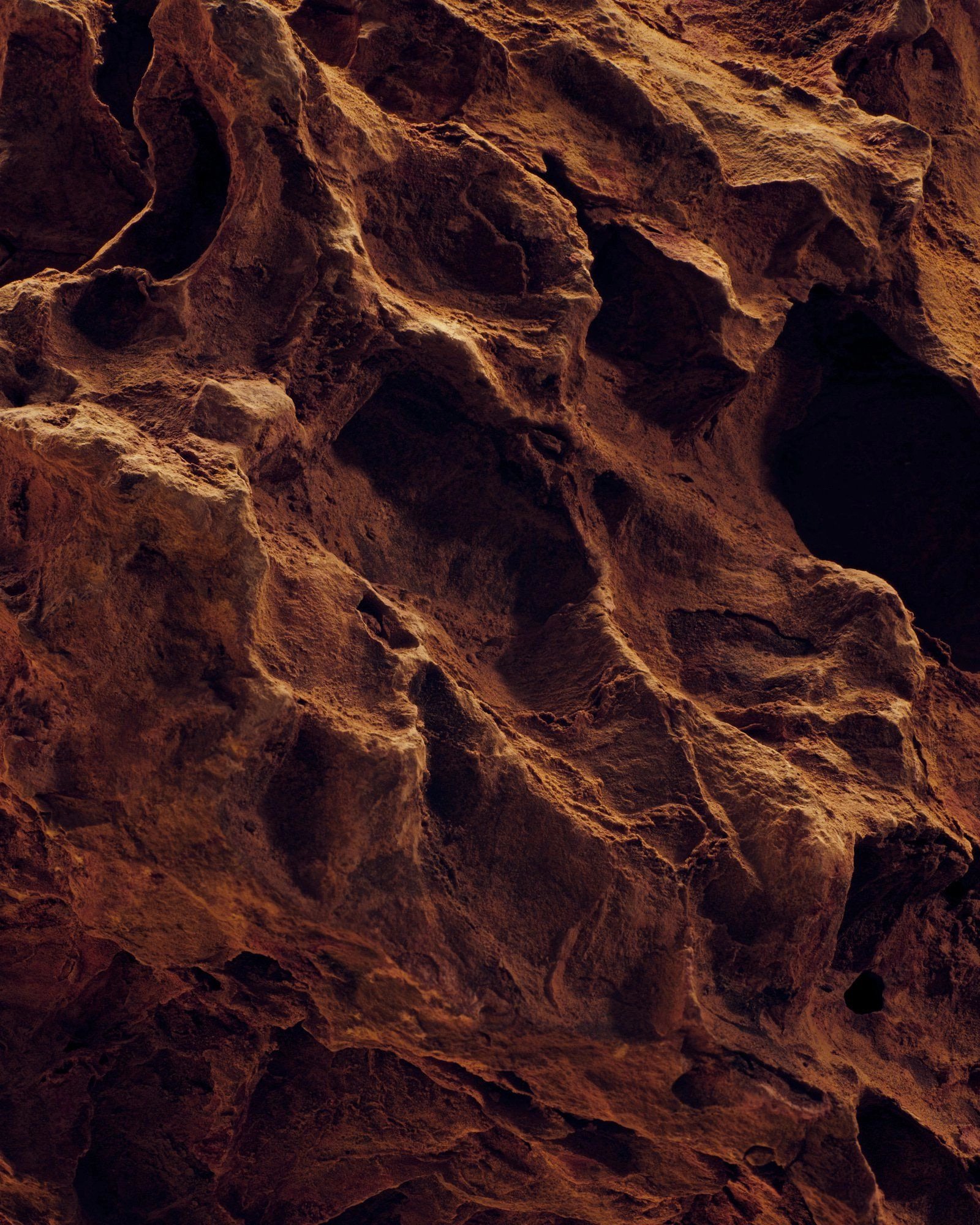 Surface of a rugged, dark brown rock formation with deep crevices and irregular texture.