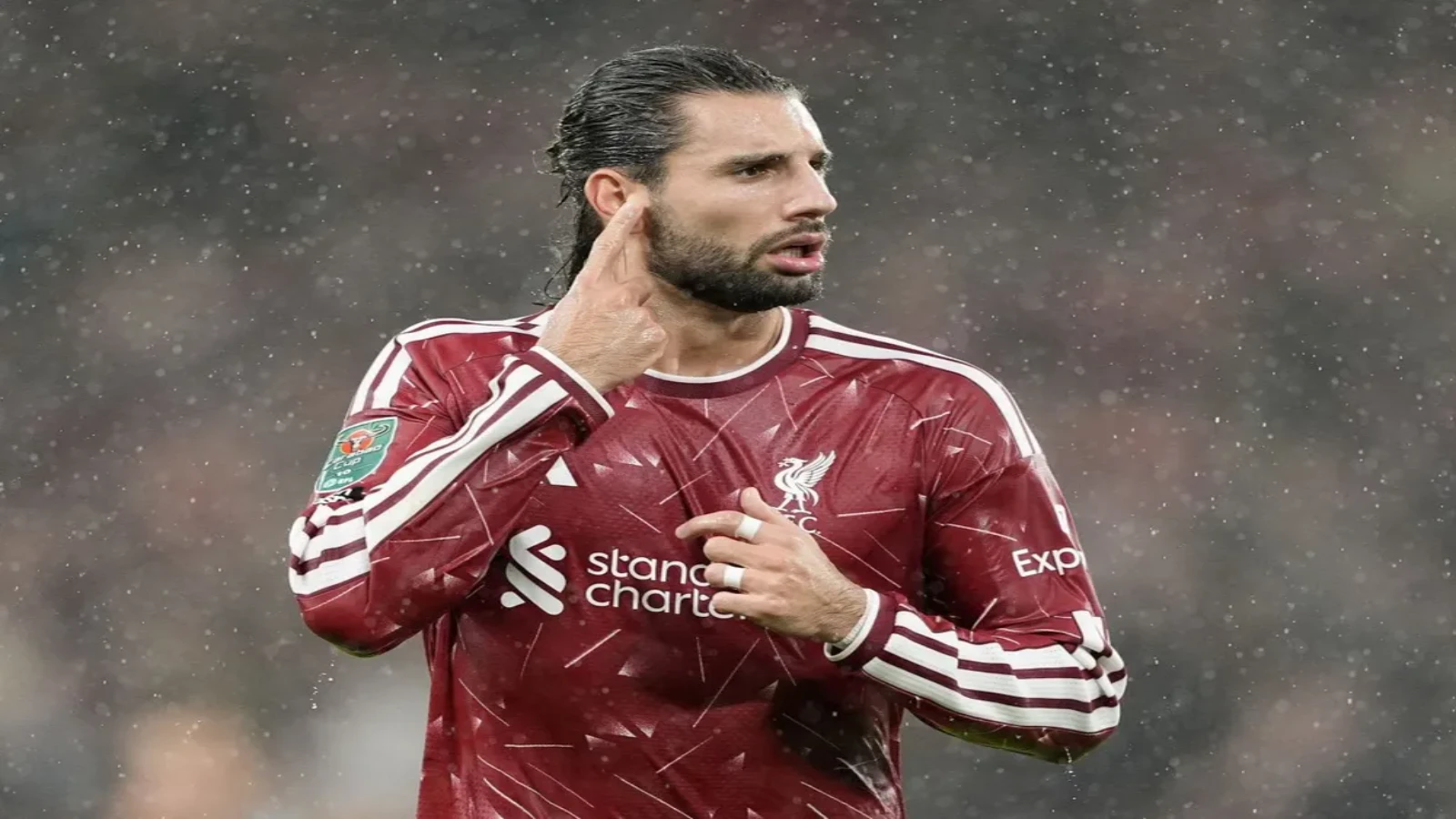 Dominik Szoboszlai points to his ear and touches the Liverpool crest on his dark red home shirt as rain falls under floodlights.
