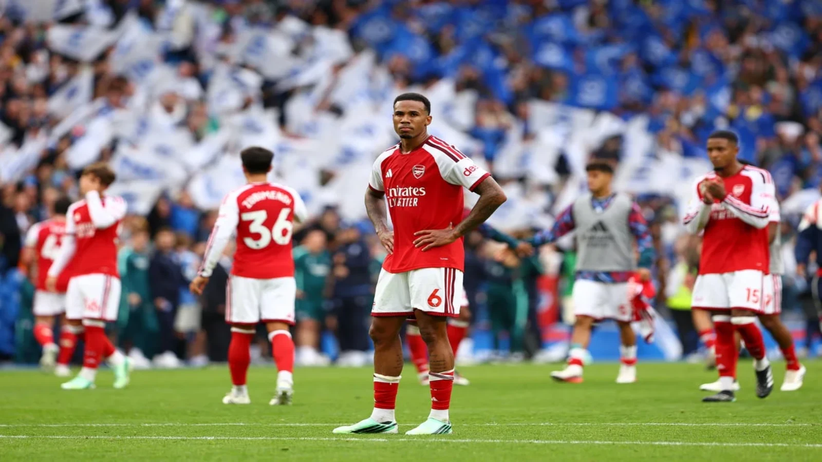 Dejected Arsenal players on the pitch as Brighton fans wave flags behind them