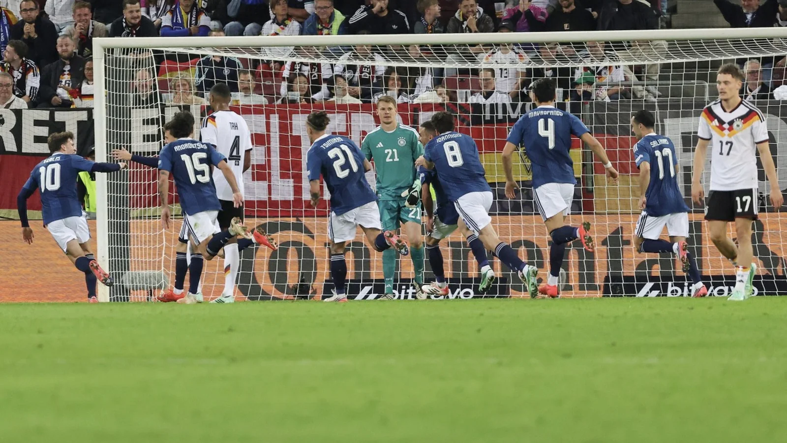 Greece players celebrate in front of Germany’s goal as German players look on.