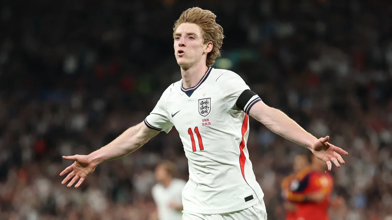 Anthony Gordon celebrates with his arms outstretched in an England shirt