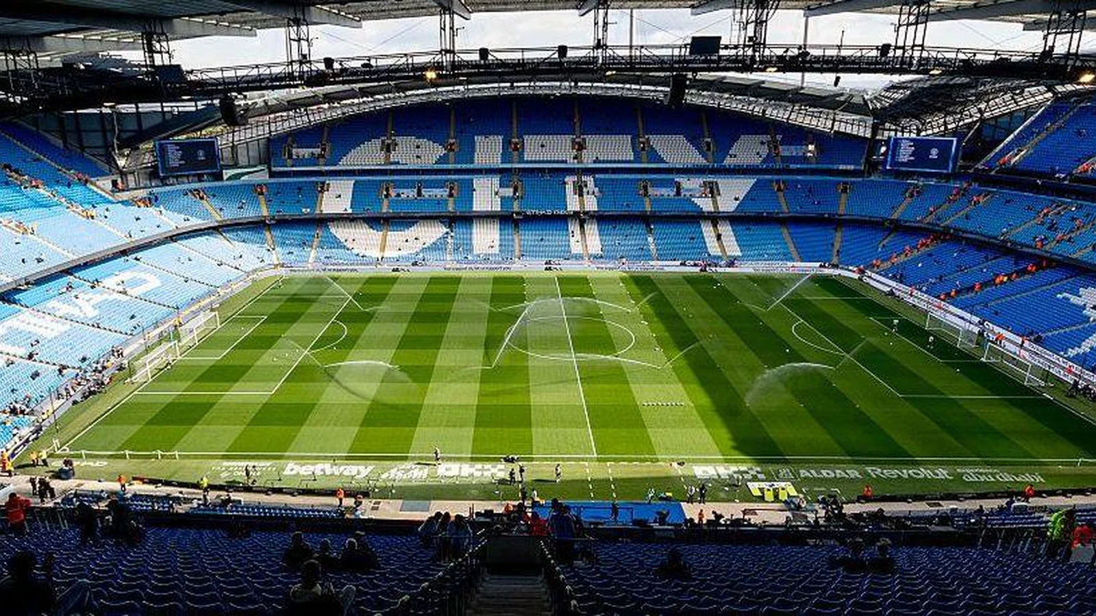 A wide view of the pitch and mostly empty blue stands at Manchester City’s Etihad Stadium.