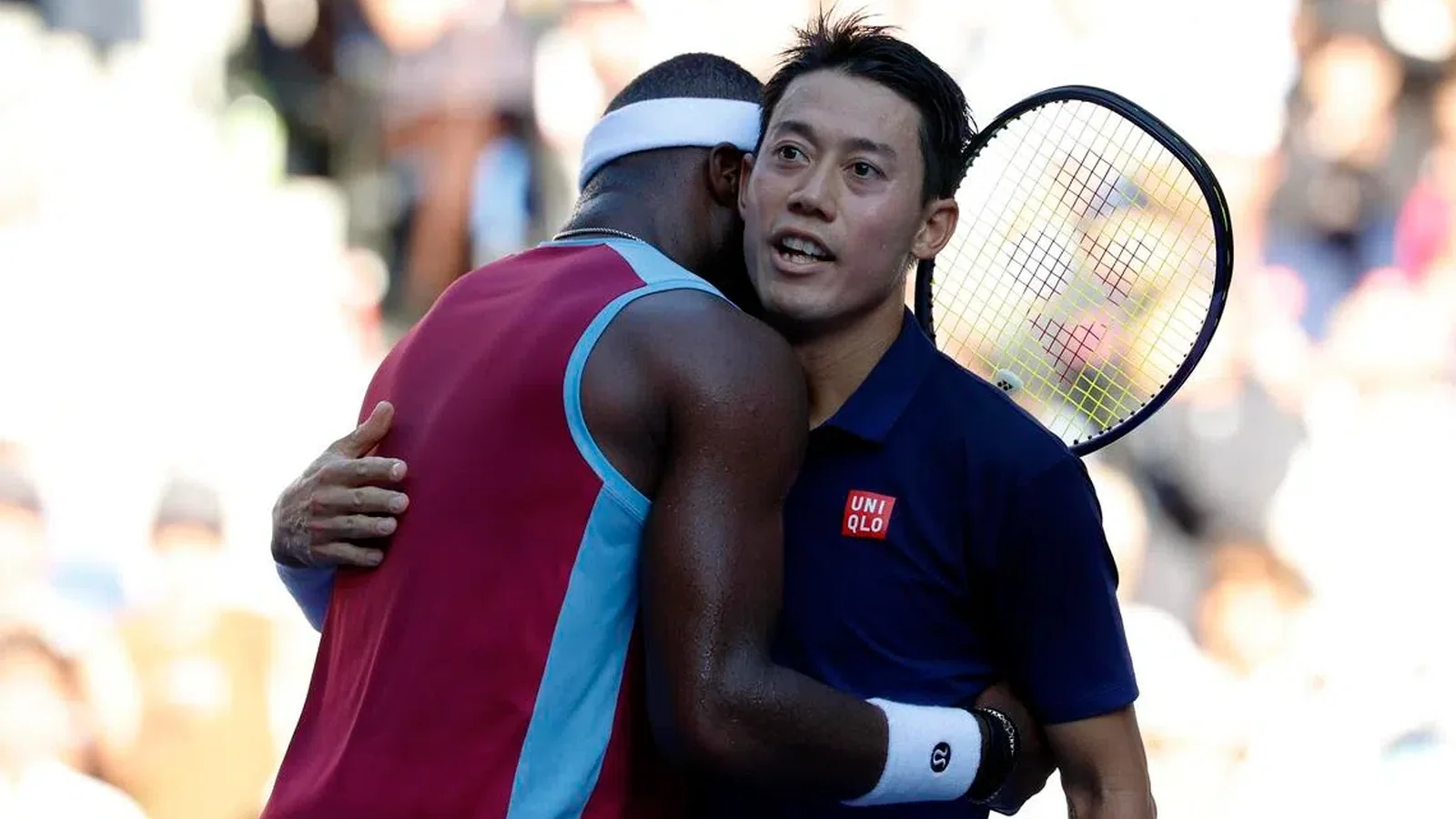Kei Nishikori in a navy shirt embracing another tennis player on court.