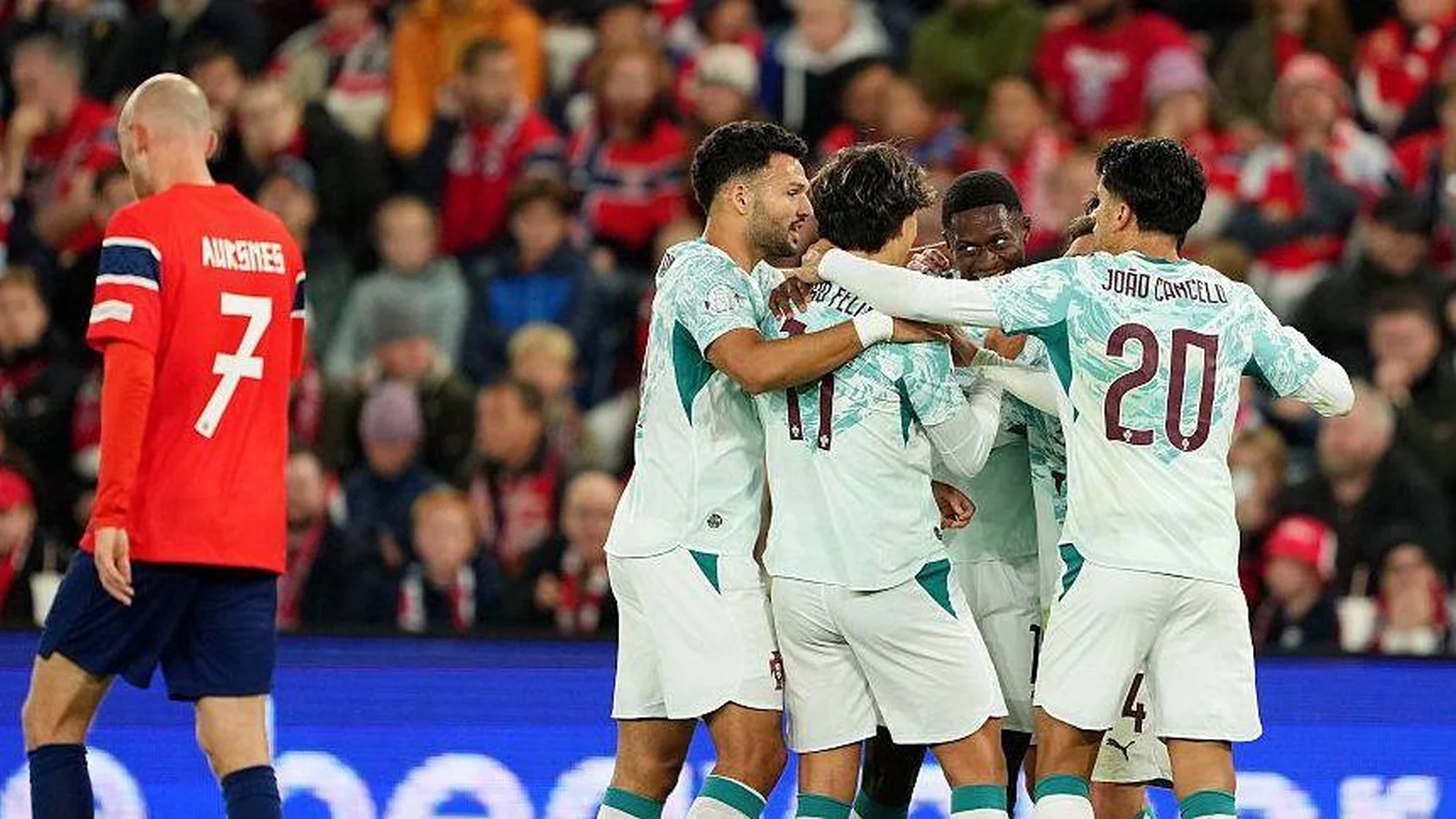 Portugal players celebrate together in white and green kits as Norway’s Fredrik Aursnes walks past.