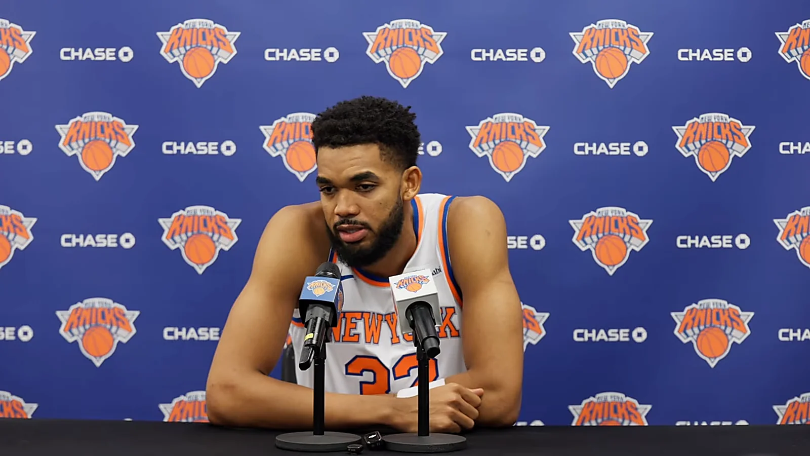 Karl-Anthony Towns speaks at a New York Knicks press conference in front of the team backdrop.