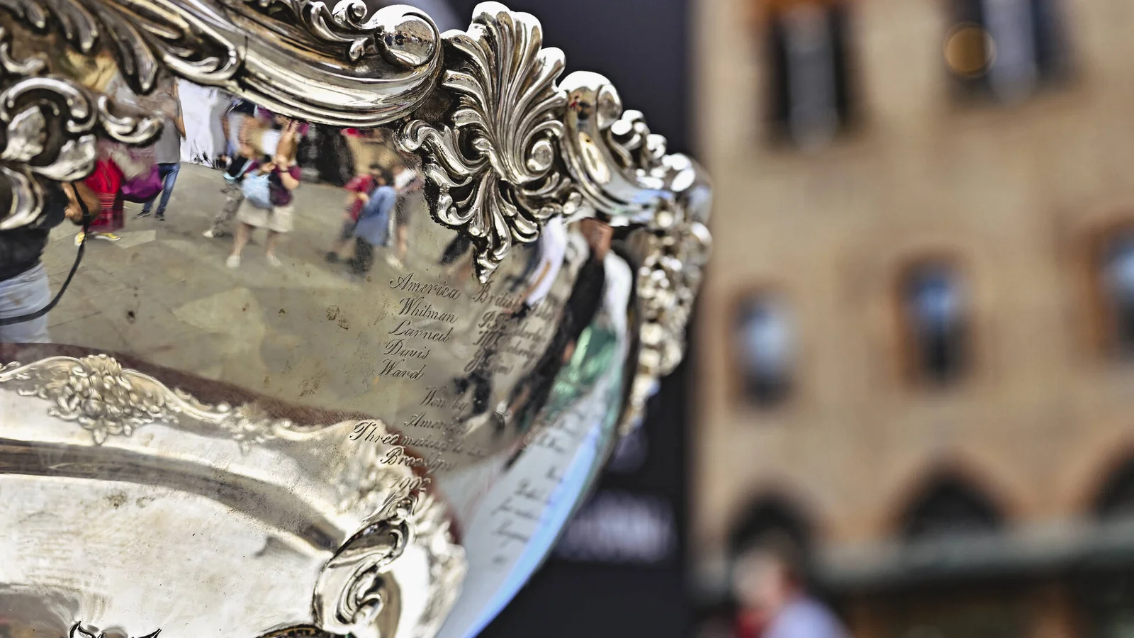Close-up of the silver Davis Cup trophy with buildings blurred in the background.