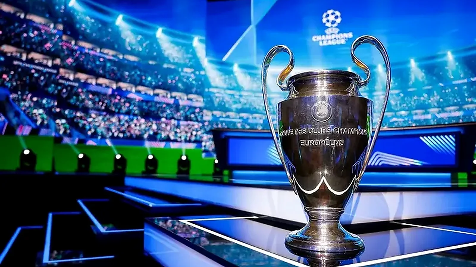 UEFA Champions League trophy displayed on stage inside a brightly lit football stadium.