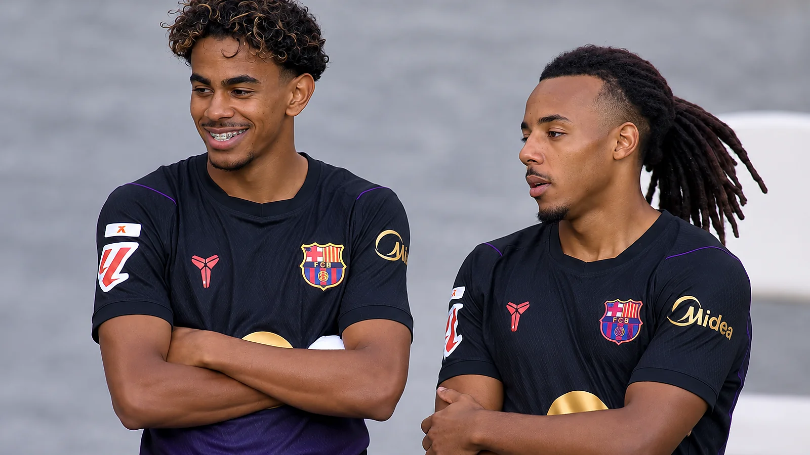 Two Barcelona players stand side by side during a match, wearing black away kits.
