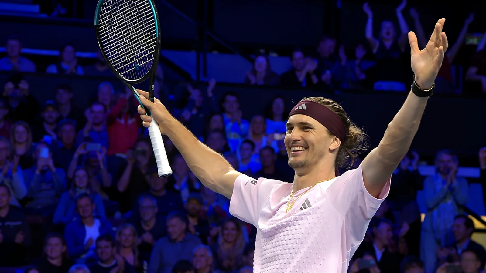 Alexander Zverev celebrates with his racket raised after a match in an indoor arena.