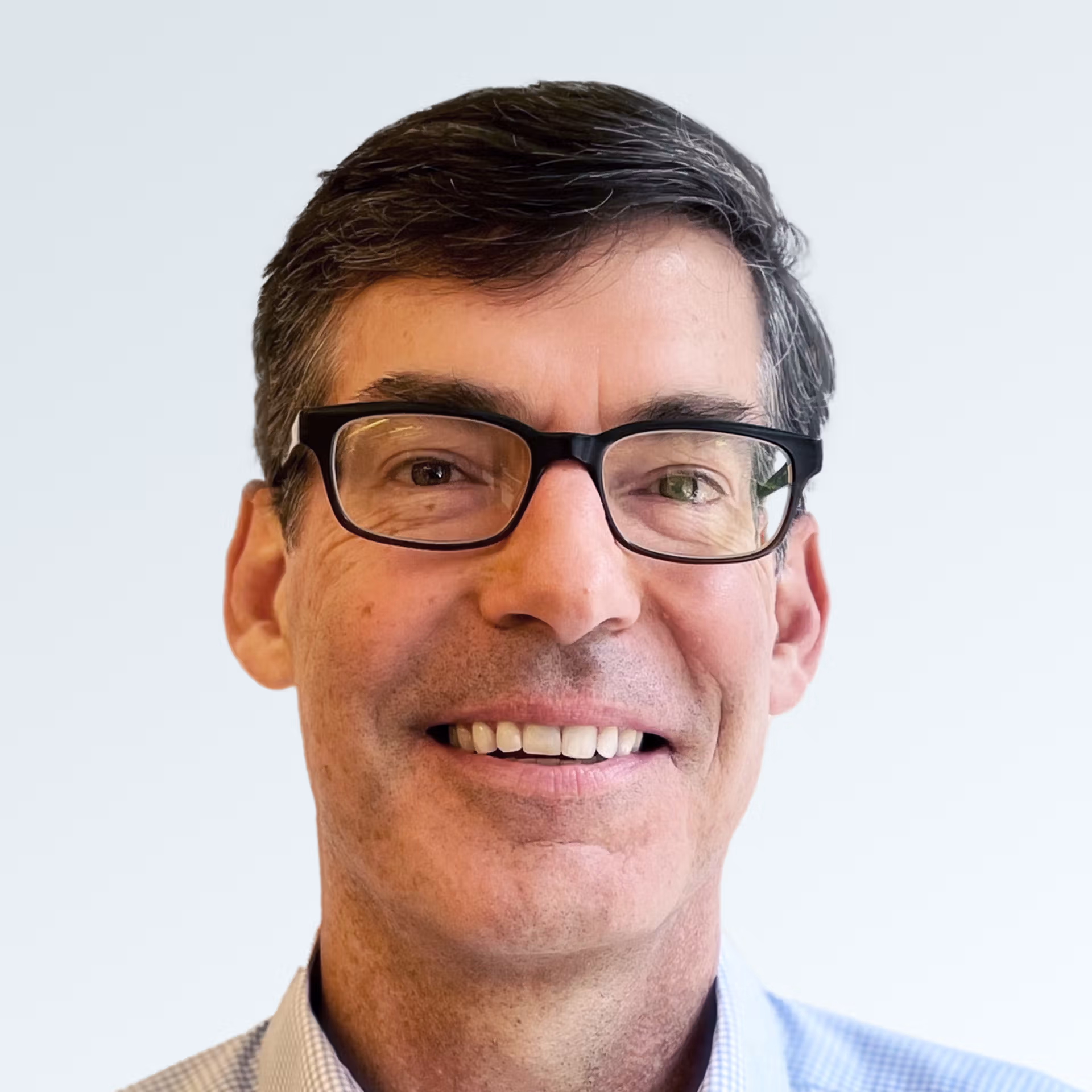Smiling middle-aged man with short dark hair, wearing black-rimmed glasses and a light blue shirt, against a plain light background.