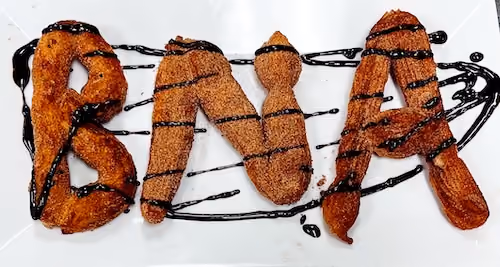 Close-up of a churro dusted with sugar, paired with a small bowl of spicy chocolate sauce, prepared during BNA's team outing at The Foodie School