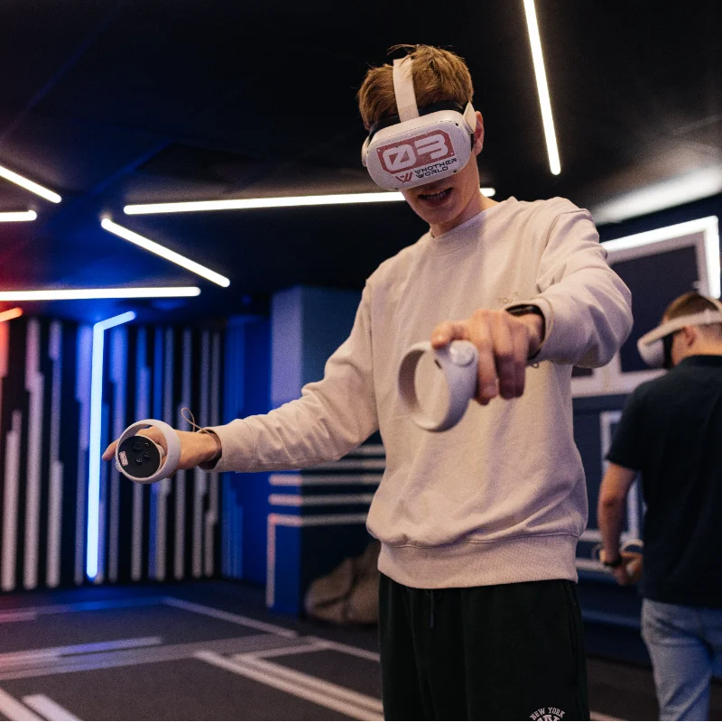 A player in a VR headset holding controllers in the lit arena