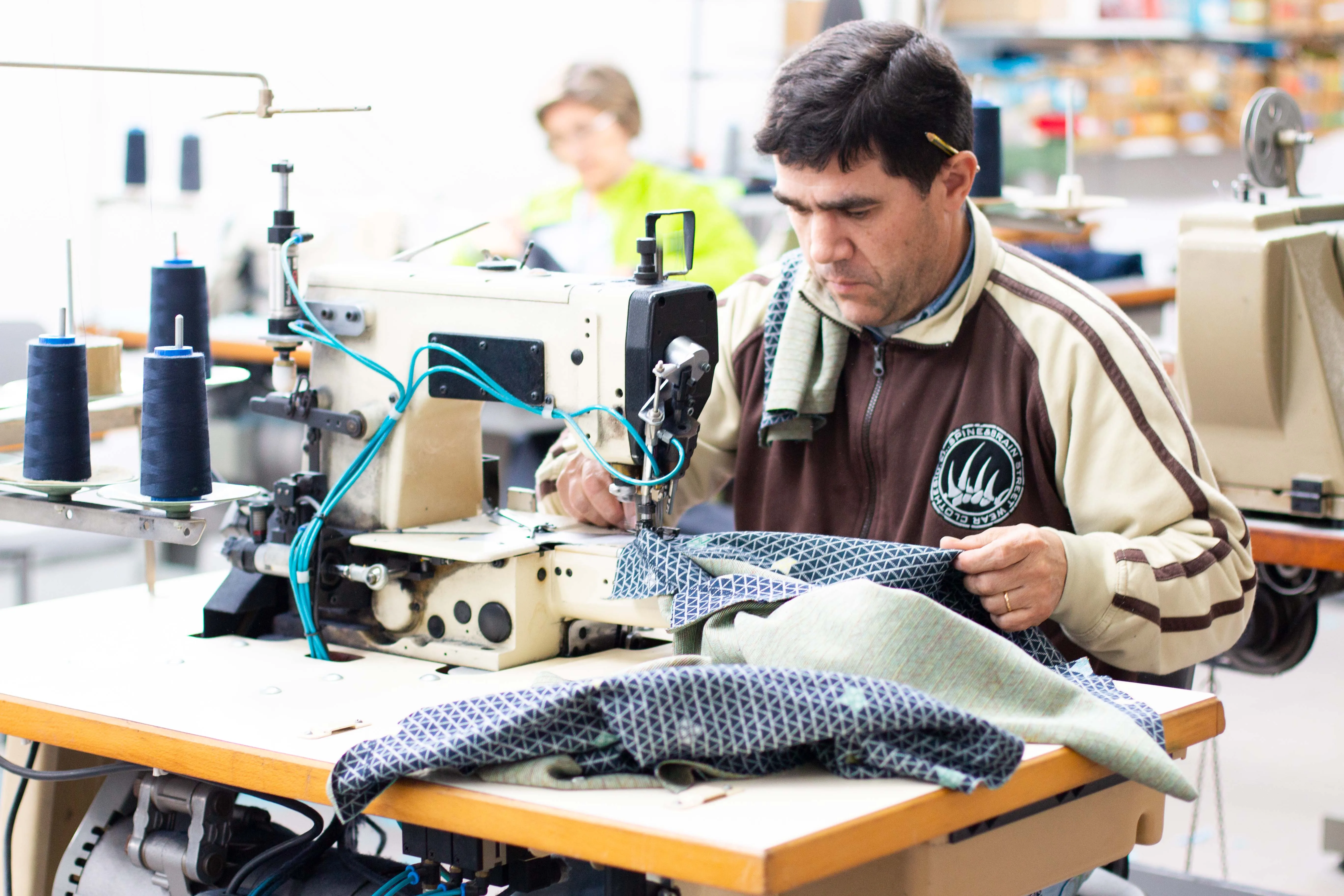 Ein Näher verarbeitet ein Kleidungsstück an einer Industrienähmaschine im Partnerbetrieb in Portugal